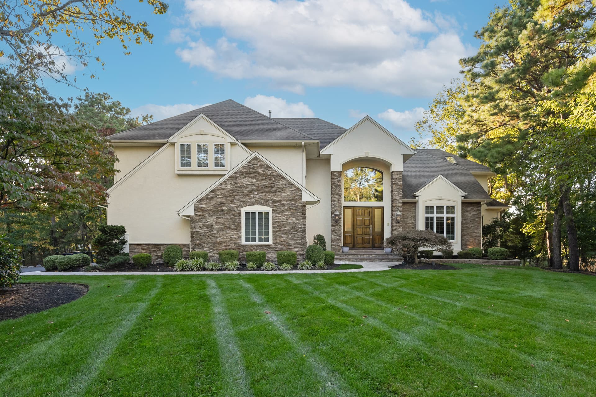 Stone and stucco custom home with a manicured striped lawn in Marlton, NJ